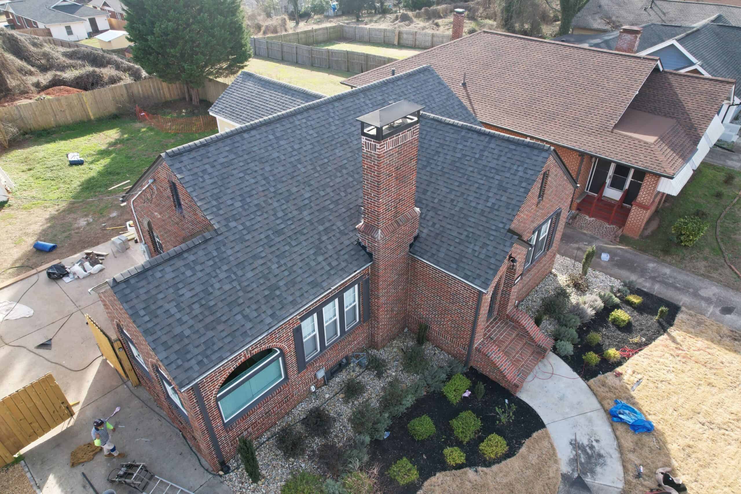 Aerial view of a renovated brick house showcasing new roofing, chimney, and landscaping in a residential neighborhood.