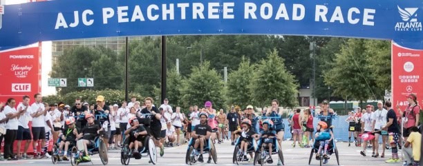 People participating in a road race event with cyclists and runners under a blue banner.