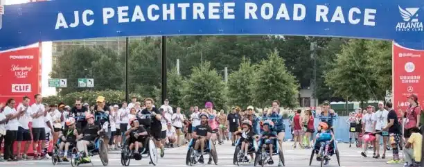 People participating in a road race event with cyclists and runners under a blue banner.
