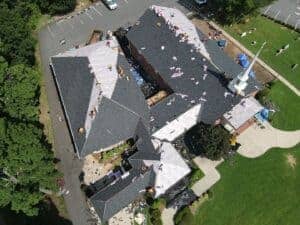Aerial view of church roof restoration, showing roofing workers replacing shingles and inspecting for damage.