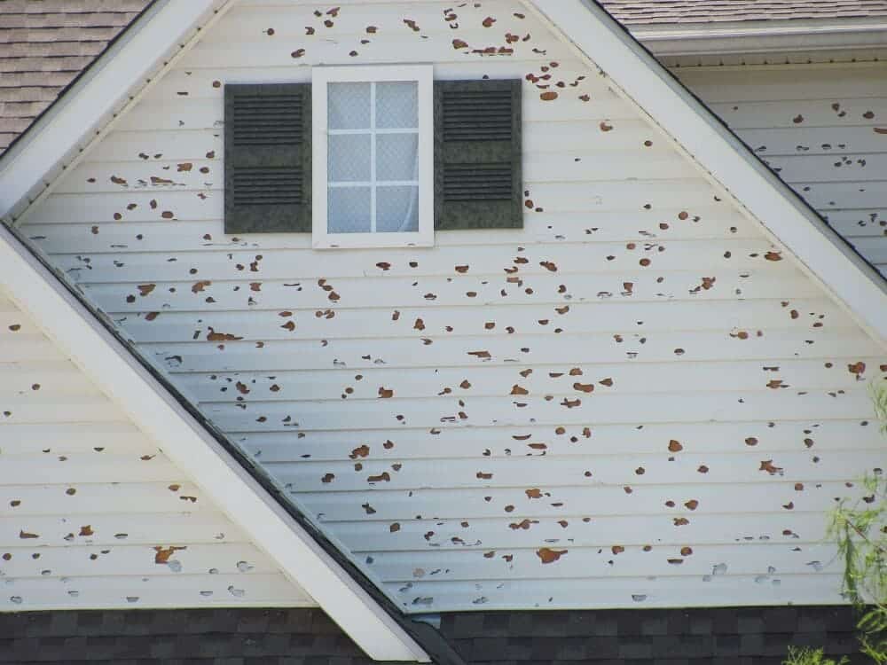 Peeling paint on house siding with small attic window in a residential roof.