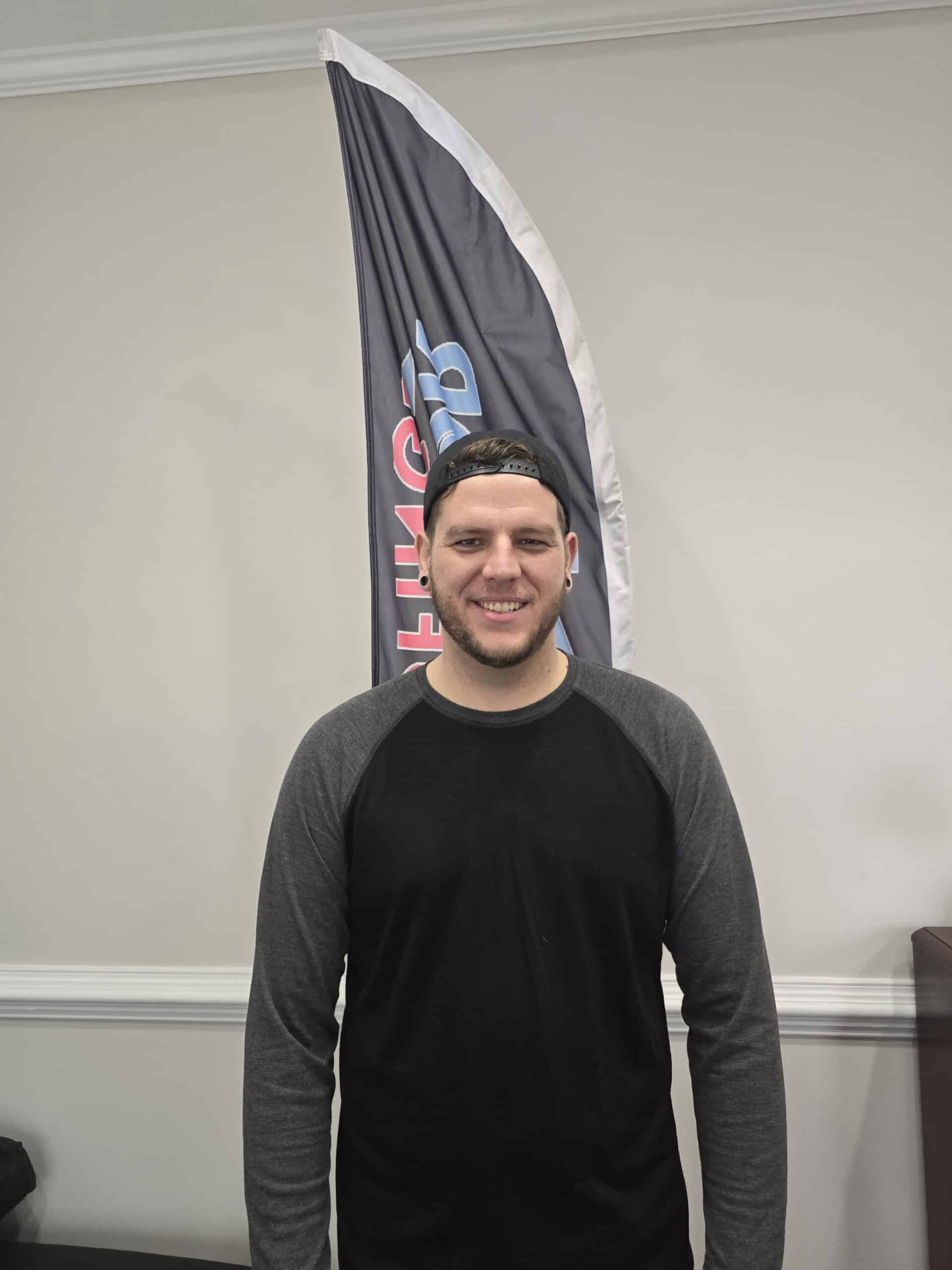 Man smiling in front of a roofing company banner during a roofing event or consultation.